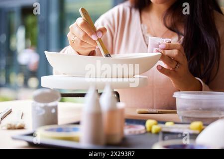 Mains, femme et peinture céramique pour la créativité, atelier d'art ou classe avec passe-temps, pinceau et matériel. Fait main, artisanat et leçon de poterie avec Banque D'Images