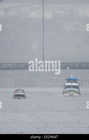 Ferry touristique et un bateau naviguant le long du fleuve Douro en passant sous le pont Don Luis I à Porto par un jour très brumeux et pluvieux. Banque D'Images