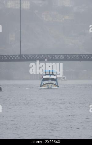 Ferry touristique naviguant le long du fleuve Douro en passant sous le pont Don Luis I à Porto par un jour très brumeux et pluvieux. Banque D'Images