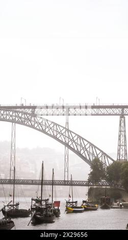 Bateaux rabelos en bois amarrés sur le fleuve Douro à Porto avec des tonneaux de vin à l'intérieur et le pont en acier Don Luis I avec des touristes se promenant avec un parapluie Banque D'Images