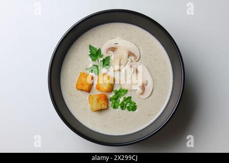 Soupe à la crème de champignons avec de la crème, des croûtons et des herbes sur un fond de bois blanc. Délicieux repas réconfortants, Banque D'Images