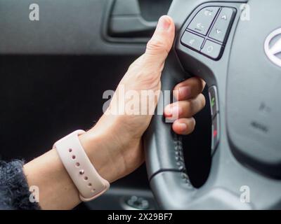 Une femme conduit une voiture avec une montre rose au poignet. Elle tient le volant des deux mains Banque D'Images