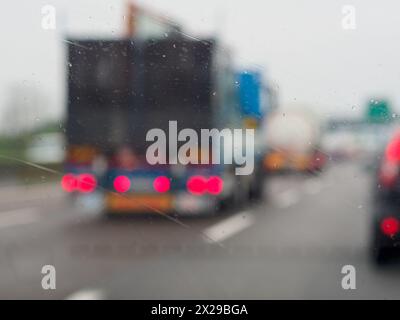 Une image floue d'une rue animée avec des voitures et un camion. La pluie mouille le pare-brise des voitures et du camion Banque D'Images