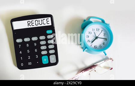 Réduire le mot écrit sur la calculatrice et fond blanc avec horloge et lunettes Banque D'Images