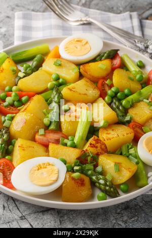 Pommes de terre frites avec asperges, tomates cerises, oeufs et petits pois gros plan dans une assiette sur la table. Vertical Banque D'Images