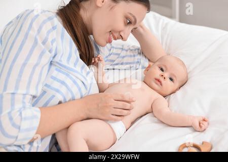 Jeune femme heureuse appliquant la crème pour le corps sur la peau du bébé sur le lit Banque D'Images