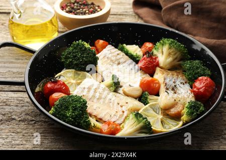 Morue savoureuse cuite avec des légumes dans une poêle à frire sur une table en bois, gros plan Banque D'Images