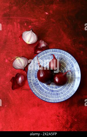 Oignon rouge sur plaque en céramique bleue, fond texturé rouge vif avec espace pour le texte. Gros plan de la texture de l'oignon. Concept d'alimentation saine. Banque D'Images