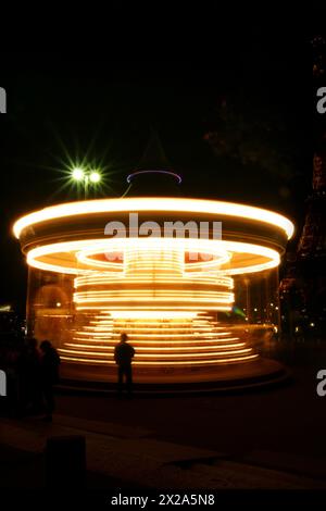 Un carrousel lumineux et tournant la nuit capturé avec une longue exposition, créant des traînées de lumière dorée vibrantes, avec la silhouette d'une personne debout Banque D'Images