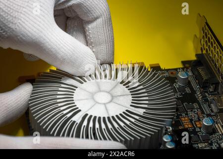 Un technicien portant des gants antistatiques blancs assemblant le radiateur de refroidissement sur la carte graphique de l'ordinateur Banque D'Images