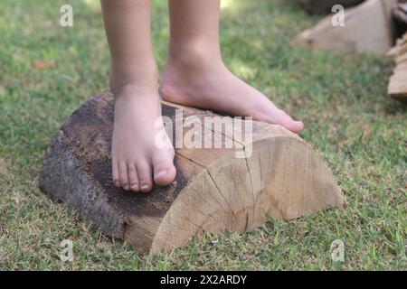 Pieds d'enfant sur bûche de bois, petite fille pieds nus sur tronc d'arbre, style de vie à la campagne, concept de mise à la terre et de connexion avec la nature Banque D'Images