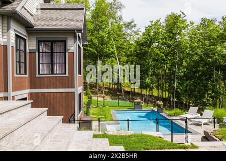 Piscine encastrée et vue arrière de pierre naturelle contemporaine, bois teinté brun et bardeaux de cèdre revêtus de luxueux bungalow en été, Quebe Banque D'Images