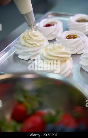 Baker ajoutant la crème anglaise du sac à pâtisserie au sommet du nid de merengue Banque D'Images