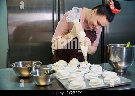 Concentré femme confiseur décorant ensemble de nids de merengue avec crème anglaise Banque D'Images