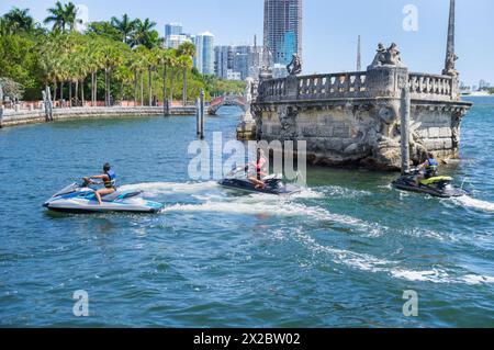 Touristes chevauchant des bateaux de jet ski dans les eaux turquoise de Biscayne Bay en face de la barge de pierre dans le quartier Coconut Grove de Miami ville sous bleu Banque D'Images