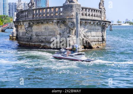 Un bateau de jet ski touriste dans les eaux turquoise de Biscayne Bay devant la barge de pierre dans le quartier de Coconut Grove de Miami ville sous bleu Banque D'Images