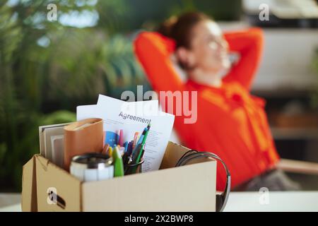 Nouvelle tâche. Gros plan sur l'employée féminine moderne heureuse dans le bureau vert moderne avec des effets personnels dans la boîte en carton. Banque D'Images