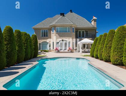 Piscine creusée bordée par des rangées de Thuja occidentallis - cèdres et dos de pierre beige avec garniture blanche maison luxueuse. Banque D'Images