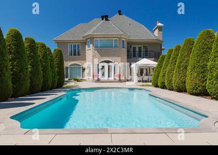 Piscine creusée bordée par des rangées de Thuja occidentallis - cèdres et dos de pierre beige avec garniture blanche maison luxueuse. Banque D'Images