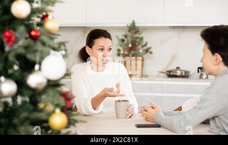 Mère et fils adolescent buvant du thé dans la cuisine et bavardant tout en célébrant Noël Banque D'Images