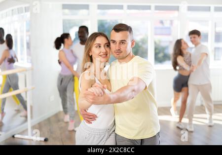 Heureux homme caucasien et fille dans les vêtements de sport dansant cha-cha-cha danse dans le studio de danse pendant la classe de groupe Banque D'Images