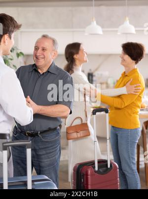 Heureux jeune couple avec des bagages venant aux parents. Homme et femme âgés accueillant joyeusement les enfants dans le couloir Banque D'Images