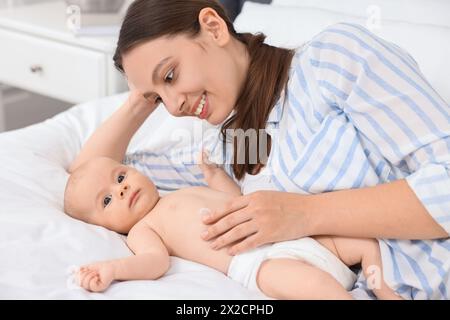 Jeune femme heureuse appliquant la crème pour le corps sur la peau du bébé sur le lit Banque D'Images