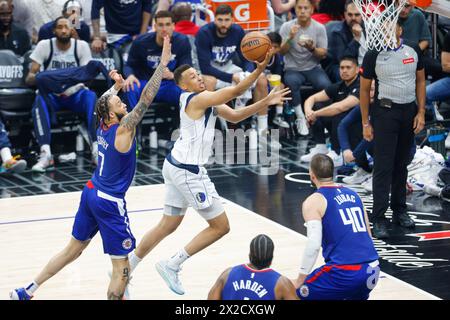 Los Angeles, États-Unis. 21 avril 2024. Dante Exum (C) des Dallas Mavericks passe devant Amir Coffey des Los Angeles Clippers (G) au panier lors d'une première manche des éliminatoires de basket-ball NBA au Crypto.com Arena. Score final : Clippers 109:97 Mavericks crédit : SOPA images Limited/Alamy Live News Banque D'Images