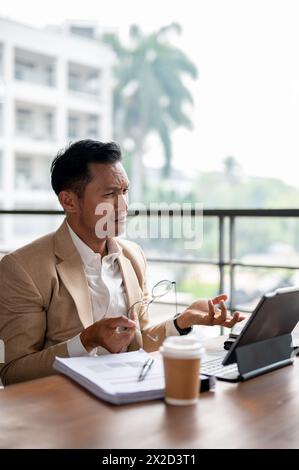Un homme d'affaires asiatique confus et sérieux regarde son écran de tablette numérique avec une expression perplexe, confronté à un problème pendant WO Banque D'Images