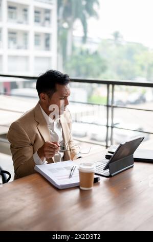 Un homme d'affaires asiatique confus et sérieux regarde son écran de tablette numérique avec une expression perplexe, confronté à un problème pendant WO Banque D'Images