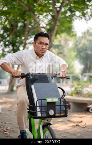 Un homme d'affaires millénaire asiatique stressé et anxieux est pressé de se rendre au travail le matin, à vélo, inquiet d'être en retard, montrant de l'urgence Banque D'Images