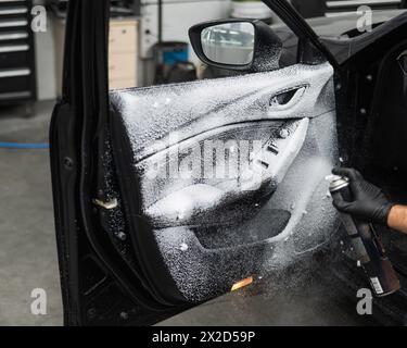 Un homme pulvérise de la mousse nettoyante sur l'intérieur d'une voiture. Banque D'Images