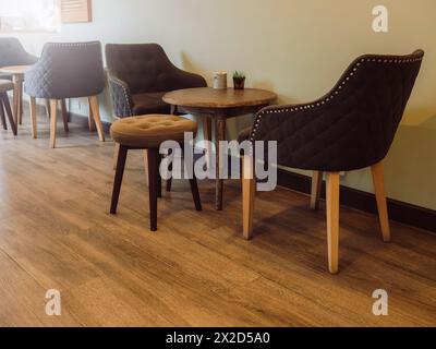 Set de table, table ronde en bois vide avec fauteuils en tissu et chaise tabouret rond en velours bouton sur plancher de bois à côté du mur Uni dans le café s. Banque D'Images