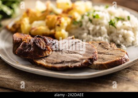 Tranches de cou rôti avec pommes de terre et riz sur une assiette - gros plan. Banque D'Images