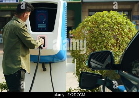 Conducteur prenant la prise d'un point public pour charger son véhicule électrique Banque D'Images