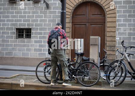 Homme avec sac à dos et Cap fixant son vélo à un poteau avec crochet et chaîne. Banque D'Images