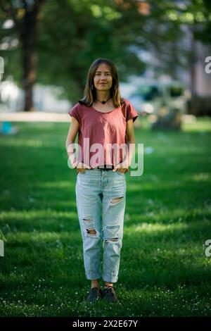 Une jeune femme portant un T-shirt et un Jean déchiré se tient dans un parc, regardant contemplativement au loin. Banque D'Images