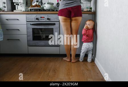 Un petit enfant se tient à côté de sa mère dans la cuisine. Banque D'Images