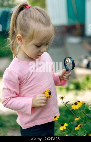 Un enfant examine une fleur sous une loupe Banque D'Images