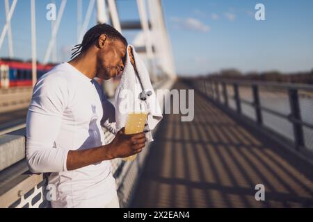 Portrait d'un jeune homme afro-américain fatigué qui essuie la sueur de son visage après le jogging. Banque D'Images