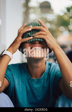 Heureuse femme riante tirant sa casquette sur ses yeux. Idiot. Banque D'Images