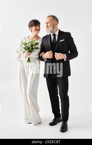 Une mariée et un marié d'âge moyen dans une élégante tenue formelle se tiennent à côté de l'autre, célébrant leur journée spéciale dans un cadre de studio. Banque D'Images