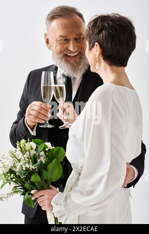 Mariés et mariés d'âge moyen en tenue de mariage, ils préparent des verres de champagne dans un studio pour célébrer leur journée spéciale. Banque D'Images