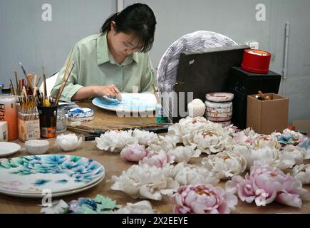 (240422) -- LUOYANG, 22 avril 2024 (Xinhua) -- Un membre du personnel fabrique un objet artisanal en porcelaine sur le thème de la pivoine au Musée de porcelaine de Luoyang à Luoyang, province du Henan en Chine centrale, 17 avril 2024. Capitale impériale pendant 13 dynasties, Luoyang prétend avoir les meilleures pivoines du pays. Ces dernières années, Luoyang a activement exploré la culture liée aux fleurs de pivoine, encourageant le développement de la porcelaine sur le thème de pivoine, la peinture et de nombreuses autres activités caractéristiques contenant des éléments de pivoine. Cela permet aux touristes de profiter à la fois des fleurs et de l'ambiance de cette ancienne capitale. (X Banque D'Images