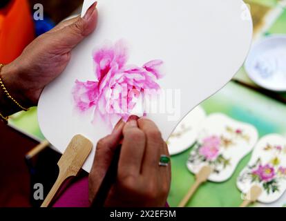 (240422) -- LUOYANG, 22 avril 2024 (Xinhua) -- Un membre du personnel décore un éventail sur le thème de pivoine dans un jardin botanique de Luoyang, province du Henan, en Chine centrale, 17 avril 2024. Capitale impériale pendant 13 dynasties, Luoyang prétend avoir les meilleures pivoines du pays. Ces dernières années, Luoyang a activement exploré la culture liée aux fleurs de pivoine, encourageant le développement de la porcelaine sur le thème de pivoine, la peinture et de nombreuses autres activités caractéristiques contenant des éléments de pivoine. Cela permet aux touristes de profiter à la fois des fleurs et de l'ambiance de cette ancienne capitale. (Xinhua/Li Jianan) Banque D'Images