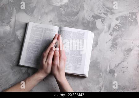 Religion. Femme chrétienne priant sur la Bible à la table texturée grise, vue de dessus. Espace pour le texte Banque D'Images