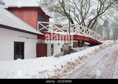 Vieille grange blanche et rouge par temps nuageux d'hiver avec des arbres sans feuilles et de la neige sur le sol. Banque D'Images