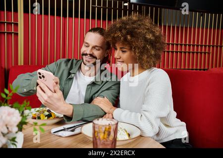 Un homme et une femme afro-américaine assis à une table, pris dans un téléphone portable. Banque D'Images