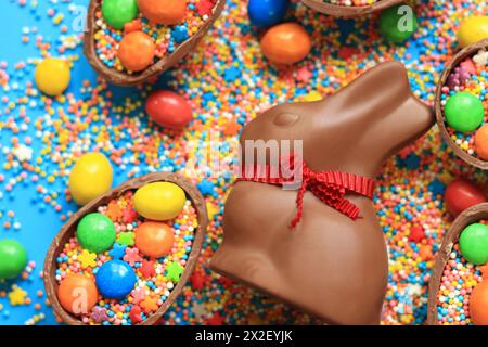 Lapin en chocolat et bonbons, saupoudres de sucre coloré sur un fond bleu, vue de dessus. Composition de Pâques. Lapin en chocolat de Pâques. Friandise festive. CH Banque D'Images