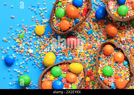 Oeufs en chocolat avec des bonbons et des saupoudres de couleur sucre sur un fond bleu, vue de dessus. Composition de Pâques. Des moitiés d'œufs en chocolat sur la table. Fes Banque D'Images